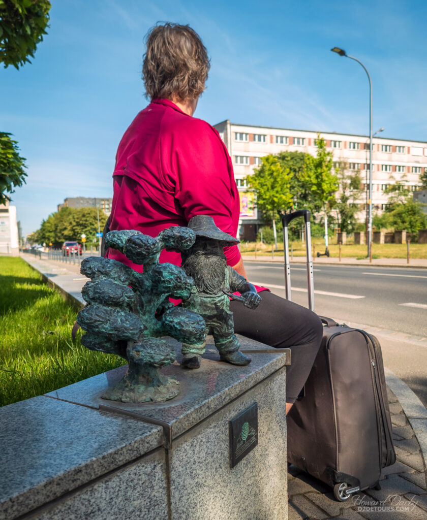 Whitney in Wroclaw sitting next to a dwarf as she waits for our cab to the bus station