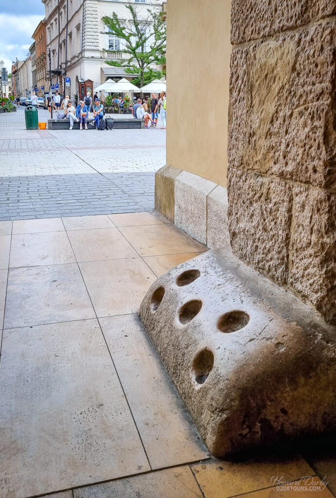 These strange holes at the base of the entrances to the Cloth Hall aren't some sort of weird umbrella stand - they are "torch sockets" used to smudge out your torch when you arrived at the hall at night